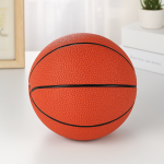 Hucha de cerámica con diseño de balón de baloncesto naranja sobre una mesa blanca