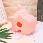 Parte trasera de una hucha con forma de cerdito rosa, mostrando la tapa inferior desmontable para sacar las monedas, diseño decorativo sobre superficie clara.