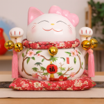 Maneki-Neko de cerámica blanco con lazo rosa, campanas doradas y decoración floral, sentado sobre un cojín rojo estampado