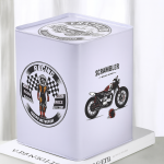 Hucha metálica blanca decorada con ilustraciones de motocicleta y casco, colocada sobre una superficie clara