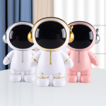 Figuritas decorativas con forma de astronauta, disponibles en blanco con detalles dorados, blanco con detalles plateados y rosa con detalles plateados, colocadas sobre una mesa.