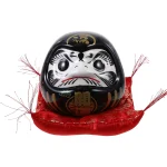 Hucha Daruma japonesa negra con base de tela roja, símbolo de fuerza, éxito y protección